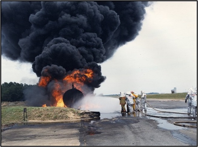 A group of firefighters putting out a fire adjacent to an aircraft runway.