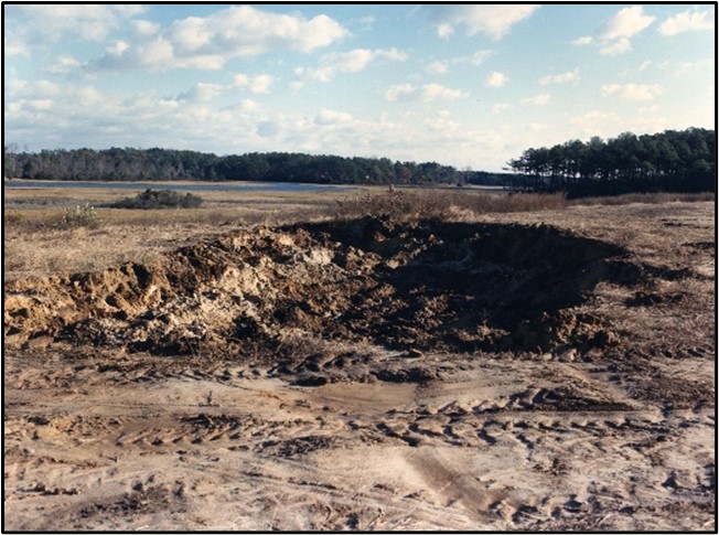 A barren field with a large hole in the center and many visible vehicle tracks.